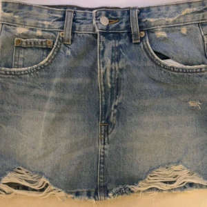 Jeanskjol - Snygg blå jeanskjol från Pull & Bear med slitna och fransiga detaljer längst ner. Klassisk jeanskjolmodell med knappstängning. Perfekt för både vardag och festliga tillfällen. Kjolen är i storlek S. 