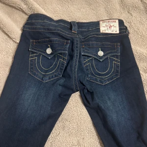 True Religion Joey Low Rise Flare Jeans - Mörkblå jeans från True Religion, modell Joey Low Rise Flare i storlek w26. Snygga kontrastsömmar, klassiska bakfickor med lock och silverfärgade knappar. Låg midja och utsvängda ben. De är i super bra skick och endast använda ca 3-5 ggr, säljer endast då de är lite för stora❣️