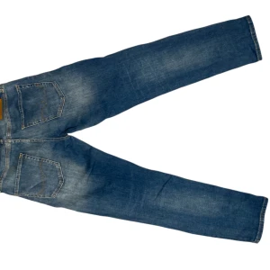 Blå tapered jeans från Jack & Jones - Snygga blå jeans från Jack & Jones i modellen Tapered/Mike vilket är slim/straight fit. Jeansen har klassisk femficksdesign, orangea kontrastsömmar och en schysst tvätt med slitningar på lår och knän. Tillverkade i bomull med knappgylf. Det är 28 i waist och 30 i längd. Tveka inte på att komma med frågor eller prisförslag🟦