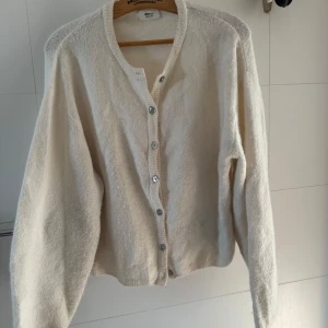 Beige kofta från Gina Tricot i ullmix - Mysig beige kofta från Gina Tricot i ullblandning. Koftan har rund halsringning, långa ärmar och knäpps framtill med silvriga knappar. Perfekt för lager-på-lager och chill höst- eller vinterstil.