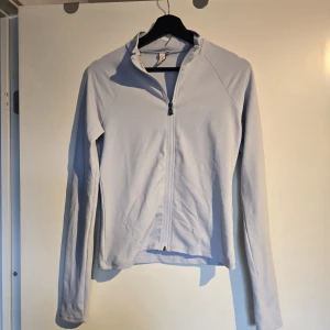 Ljusblå ziptröja med lång ärm - Ljusblå ziptröja med hel dragkedja framtill och lång ärm. Tröjan har en enkel, clean design med smal passform och stårkrage. Perfekt för dig som gillar minimalistisk stil och vill ha något lätt att slänga på sig.