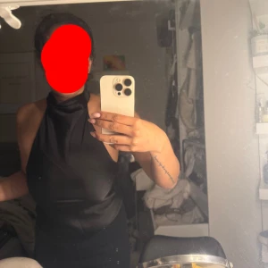 Svart halterneck top strl 34 - Snygg svart top  med halterneck och öppen rygg. Topen har en slät, figurnära passform och ärmlös design som ger en cool och elegant vibe. Perfekt för dig som gillar minimalistisk stil och vill sticka ut med en stilren look.