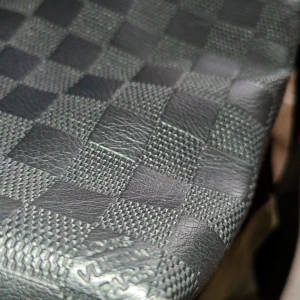  axelväska i svart skinn - Snygg axelväska i svart skinn med klassiskt rutigt mönster. Väskan har justerbar axelrem, lock med präglad logga och dragkedjefack på framsidan. Perfekt för dig som vill ha en stilren och praktisk väska med lyxig känsla.