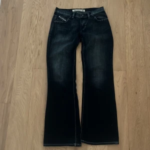 Low waist Vintage Diesel bootcut jeans i mörkblå denim - Snygga vintage mörkblå jeans från Diesel med bootcut passform och klassiska kontrastsömmar. Jeansen har fem fickor, diskreta slitningar och detaljer med röda Diesel-loggor. Jeansen är vit tvättade och i bra skick. Jeansen är köpta runt 2000 talet.