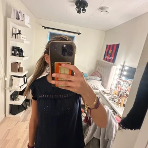 Mörkblå blus med spetsdetaljer - Säljer en mörkblå blus med fina spetsdetaljer och små hålmönster framtill. Blusen har korta ärmar med volang och en avslappnad passform. Perfekt för dig som gillar en söt och stilren look.