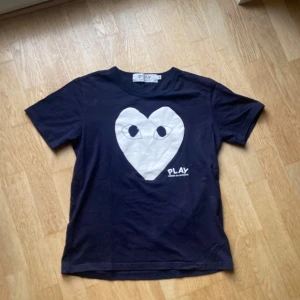  Comme des Garçons Play t-shirt - Cool mörkblå t-shirt från Comme des Garçons Play med stort vitt hjärta och ögon på bröstet. Klassisk rund hals och korta ärmar. Perfekt statement-plagg för dig som gillar streetwear och snygga prints. Medium men passar S/Xs