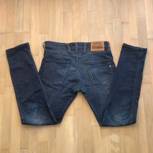 Replay Anbass - Snygga blå jeans från Replay, modell Anbass med slim fit. De är i väldigt bra kvalitet utan några märkbara defekter. Jeansen är tillverkade i stretchigt denim för extra komfort och har raka ben med smal passform.