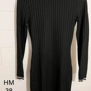 Svart ribbad klänning från H&M - Svart ribbad klänning från H&M i figurnära modell med lång ärm. Klänningen har diskreta vita ränder på ärmsluten och är tillverkad i mjukt stretchigt material. Perfekt för dig som gillar en enkel men stilren look.