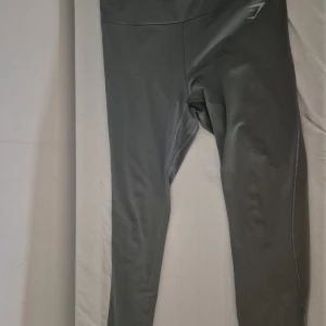 Grå leggings från Gymshark XL - Säljer ett par grå leggings från Gymshark i storlek XL. De är tillverkade i ett stretchigt material med 88% polyester och 12% elastan. Hög midja och diskret logga på benet. Perfekta för träning eller chill dagar.