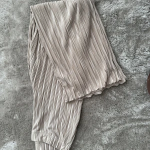 Beige plisserade byxor - Säljer ett par snygga beige plisserade byxor med elastisk midja och avslappnad passform. 