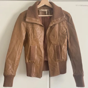 Brun skinnjacka från Vero Moda - Snygg brun skinnjacka från Vero Moda med ribbade muddar och krage. Jackan har dragkedja framtill, två fickor och coola sömdetaljer. Perfekt för dig som vill ha en klassisk men trendig look. Storlek M, men passar mig fint som hat vanligtvis S-xs