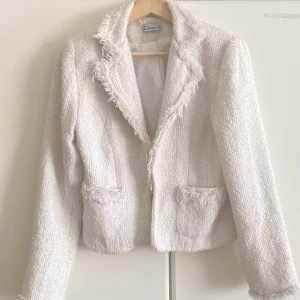 Vit kavaj från Sorbet med fransdetaljer - Stilren vit kavaj från Sorbet i strukturerat tyg med fransade kanter vid krage, fickor och ärmslut. Kavajen har två fickor framtill och är helfodrad för extra komfort. Perfekt för dig som vill ha en chic och trendig look. Storlek M men passar mig med storlek S