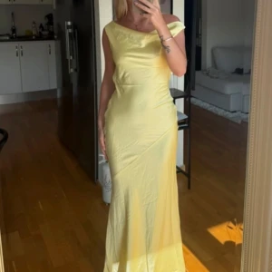 Peppermayo klänning  - Superfin ljusgul långklänning med offshoulder och snygg öppen rygg med knyt. Klänningen har en elegant, figurnära passform och är tillverkad i ett glansigt, mjukt material som faller snyggt. Perfekt för dig som vill sticka ut med en fräsch och somrig look.