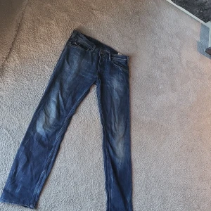 Blå Diesel Kander jeans W32 L32 - Säljer ett par blå Diesel Kander jeans med snygg tvätt och klassiska fem fickor. Jeansen har raka ben och normal passform, med läderpatch bak i midjan och diskreta slitningar framtill. Sitter riktigt Nice på kroppen, perfekt för dig som vill ha en stilig look.