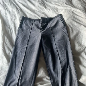 Grå kostymbyxor från Axel Arigato - Snygga grå kostymbyxor från Axel Arigato i 100% virgin ull. Byxorna har pressveck, raka ben och klassisk passform. Perfekta för dig som vill ha en clean och stilren look. Fickor i sidorna och diskret logga bak.