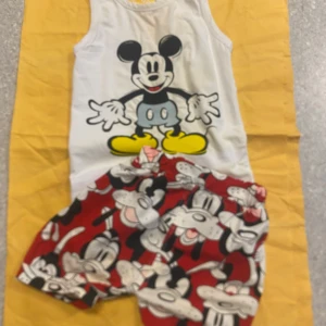 Röda Disney-shorts med Musse Pigg väst  - Färgglada röda shorts med Musse Pigg-tryck över hela tyget. Perfekta för dig som älskar tecknade figurer och vill sticka ut. Shortsen har en lös passform och elastisk midja för extra komfort.