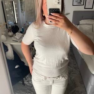 Vit kortärmad t-shirt från Zara - Vit t-shirt från Zara med rund hals och korta ärmar. Modellen är enkel och stilren med ribbad kant nedtill och vid ärmslut. Materialet känns mjukt och skönt mot huden, perfekt för dig som gillar cleana och fräscha looks.