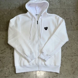 Vit Cdg play ziphoodie - Säljer denna vita zip-tröjan från Cdg play i storlek M, sjukt mjuk på insidan och logga fram med tryck på ryggen. 10/10 skick och fraktar inom 24h✅