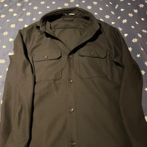 Svart overshirt från Zara, storlek S - Stilren svart overshirt från Zara med klassisk krage, två stora bröstfickor med lock och knappar framtill. Skjortan har lång ärm och en rak, något loose passform. Perfekt att bära öppen eller stängd för en cool look. Använd endast 1 gång!!Hör gärna av dig vid frågor eller funderingar angående priset!