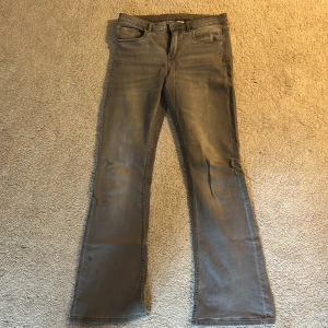 Grå bootcut jeans från Kappahl - Snygga grå jeans från Kappahl i bootcut-modell. Klassisk femficksdesign med bälteshällor och dragkedja. Jeansen har en rak passform upptill och utsvängda ben, vilket ger en cool siluett. Perfekta för dig som gillar en avslappnad men trendig look.