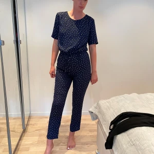Jumpsuit  - Mörkblå jumpsuit med guld prickar och snörning i midjan. Byxorna har rak passform och är croppade vid ankeln. lätt känsla som passar perfekt för en chill och snygg look.