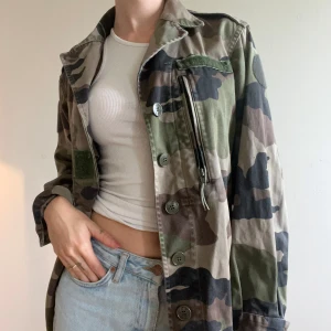 Camouflage jacka - Stilren klassisk camojacka. Jackan har långa ärmar och elastisk nederkant bak för en avslappnad look. Perfekt för dig som gillar streetstyle och utility-vibe. Passar storlek xs-m