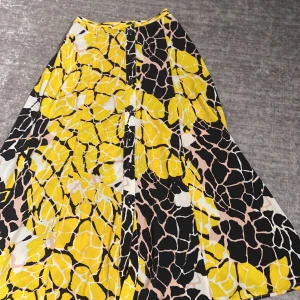 Färgglad långkjol från Lindex XS - Säljer en långkjol från Lindex i storlek XS med ett unikt mönster i gult, svart, vitt och beige. Kjolen har knappar framtill och ett flowigt fall. Perfekt för dig som gillar färg och vill sticka ut lite extra.