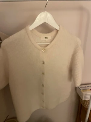 Beige stickad kofta från Gina tricot - Mysig beige stickad kofta från gina med rund hals och knappar framtill. Koftan har en enkel och clean design med ribbad struktur och lång ärm. Perfekt att slänga på sig när det är lite kyligt ute.