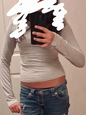 Ljusgrå långärmad topp med öppen rygg - Säljer en ljusgrå långärmad topp. Toppen har en tight passform och en snygg öppen rygg som ger en cool touch. Rundad halsringning fram och djupare skärning bak. Perfekt att matcha med jeans eller kjol. Andvänd en gång!