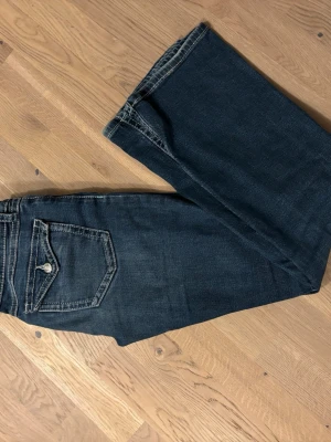 Mörkblå jeans med kontrastsömmar - Snygga mörkblå jeans från Gina Tricot med kontrastsömmar och detaljerade fickor med knapp framtill. Klassisk femficksmodell och normal passform. Jeansen har en rak siluett och är tillverkade i slitstarkt denimtyg.