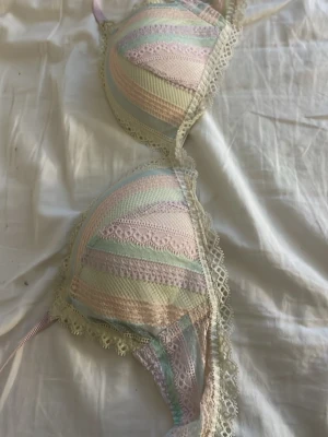 Pastellfärgad spetsbh från Intimissimi - Säljer en unik bh från Intimissimi med pastellfärgade ränder i rosa, blått, grönt och lila. Västen har spetsdetaljer längs kanterna och en mjuk, feminin look. Materialet är en blandning av spets och syntet, med justerbara axelband i ljusrosa.