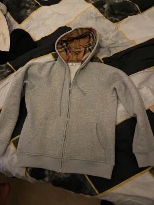 Zip Burberry Hoodie  - Säljer en helt ny och oanvänd Burberry zip hoodie i storlek S. Hoodien är grå och tillverkad i ett mjukt och bekvämt material med hög kvalitet, perfekt för både vardag och mer uppklädda outfits. Klassisk Burberry-design med dragkedja framtill och en stilren passform. Aldrig använd, i nyskick.  Passar dig som vill ha en exklusiv och bekväm hoodie med tidlös stil. 