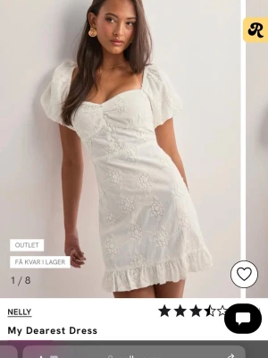 Vit kort klänning med broderade blommor - Supersöt vit kort klänning från Nelly med puffärmar, broderade blommor och volangkant nertill. Klänningen har v-ringning, knappar framtill och en öppen rygg. Perfekt för sommarens alla tillfällen! Prislapp är kvar och klänningen är aldrig använd då den är för stor 