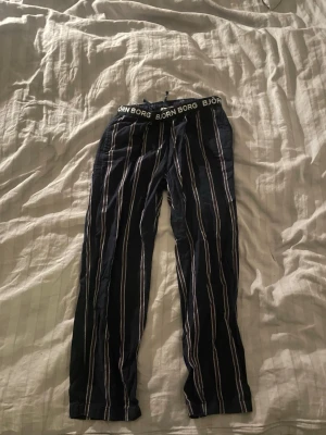 Randiga pjamas/linnebyxor från Björn Borg -  Säljer ett par mörkblå pjamas/mjukisbyxor från Björn Borg med vita och röda vertikala ränder. Byxorna har elastisk midja med snörning och logotypen tryckt på linningen. Sköna och avslappnade, perfekta för chill dagar hemma men även utomhus på varmare dagar                                                                       Storlek 146/152.         Pris kan såklart diskuteras Vid frågor  är det bara att skickar ett dm! 