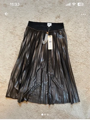 Svart plisserad kjol från Saint Tropez - Säljer en svart, glansig plisserad långkjol från Saint Tropez i storlek S. Normal i storlek.Kjolen har ett brett elastiskt midjeband och är tillverkad i 100% polyester. Perfekt för dig som gillar metallic vibes och vill ha en kjol med snyggt fall. Oanvänd!