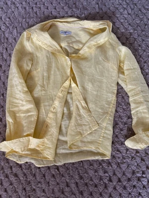 Ljusgul linneskjorta från Hampton Republic - Fräsch ljusgul skjorta från Hampton Republic i storlek 36. Tillverkad i svalt linne, med klassisk krage och långa ärmar. Skjortan har knappar framtill och en stilren, enkel design som är perfekt för varmare dagar.