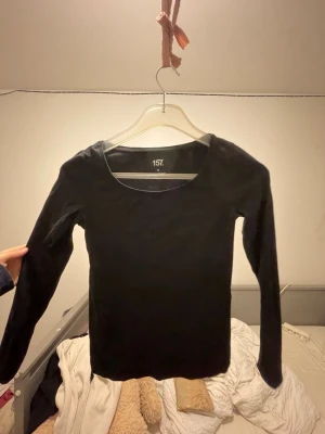 Svart långärmad topp från 157 - En enkel svart långärmad topp från 157 i storlek XS. Toppen har rund halsringning och är gjord i mjuk bomull med lite stretch för skön passform. Perfekt att styla med jeans eller kjol för en clean look.