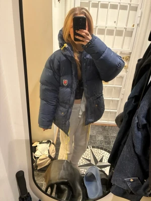 Mörkblå dunjacka från Fjällräven - Säljer en mörkblå dunjacka från Fjällräven. Jackan är i ett väldigt bra skick förutom att hängaren är trasig. Annars är jackan super fin och varm.