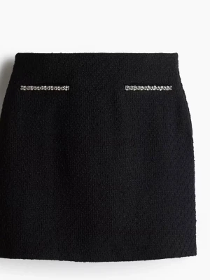 Svart kortkjol med pärldetaljer - Snygg svart kortkjol med två rader glittrande pärldetaljer framtill. Kjolen har en rak och stilren form. Från HM och den är aldrig använd. Ord pris 399kr 