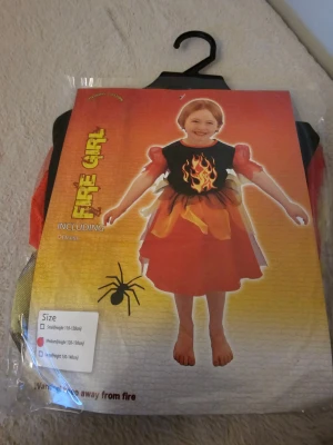 Fire Girl väst i rött och gult - Cool väst för barn med eldtema, perfekt till maskerad. Västen är svart med tryckt eldflamma framtill och har detaljer i rött, gult och orange. Tillverkad i 100% polyester och har en klassisk västform som passar över en tröja eller klänning.