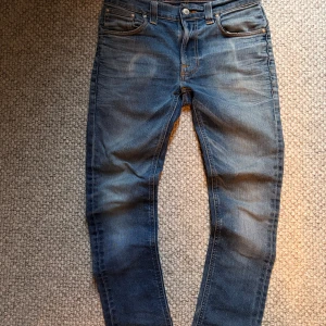 Blå slim jeans från Nudie Jeans - Säljer ett par blå slim jeans från Nudie. Jeansen har slitningar och snygga detaljer på bakfickorna med Nudie-loggan. Hör av er vid fler frågor! 