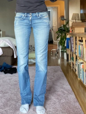 Lågmidjade Diesel bootcut jeans ljusblå - Säljer ett par ljusblå lågmidjade Diesel Ronhoir jeans med bootcut-snitt. Jeansen har klassisk femficksdesign, stretchmaterial och snygga slitningar framtill.  Storlek w28 l34 midjemått 38cm innerbenslängd 85cm