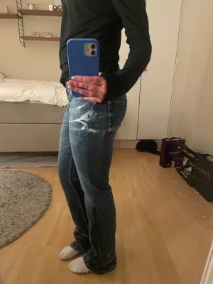 Blå bootcut jeans från Denham - Säljer ett par blå jeans från Denham med bootcut-snitt och coola slitningar framtill. Jeansen har stora bakfickor och klassisk femficksdesign. Materialet är jeans och färgen är en snygg tvättad blå med ljusare detaljer. Perfekt för dig som gillar avslappnad stil. de e sydda lågmidjade och boocut. 29/L32