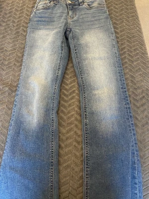 Blå jeans med raka ben - Snygga blå jeans med raka ben och klassisk femficksdesign. Jeansen har ljusa slitningar framtill och bakfickor med lock och knappdetaljer. Passar dig som gillar en enkel och tidlös look. Materialet är robust denim som håller formen.