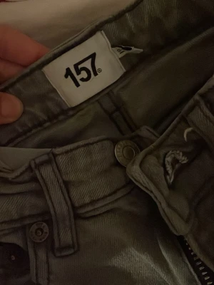 Grå jeans från 157, straight fit - Snygga grå jeans från 157 med klassisk femficksdesign och raka ben. Jeansen har dragkedja i gylfen och tydliga sömmar längs fickor och ben. Perfekt för dig som gillar en enkel och stilren look. Materialet är slitstarkt jeans och färgen är en neutral gråton.