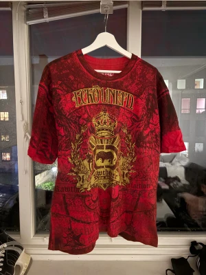 Ecko Unltd t-shirt  - Säljer en fet röd t-shirt från Ecko Unltd i storlek Large. Den har ett stort, detaljerat guld- och svart tryck med krona, döskallar och logga både fram och bak. Materialet är 100% bomull och modellen är loose fit. Perfekt för dig som gillar drainer stilen