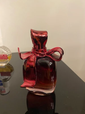 Elegant parfym med röd rosett - Snygg parfymflaska med unik röd rosett-design. Perfekt för dig som vill sticka ut med din stil. Ingen information om ingredienser, volym eller tillverkningsland syns på bilden.