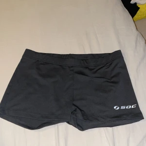 Svarta träningsshorts från SOC - Svarta träningsshorts från SOC med TCS Air-teknologi. De har en enkel och slim passform med elastisk midja. Materialet är syntet och känns lätt och smidigt, perfekt för intensiva träningspass. Diskret logga på framsidan och vid midjan.