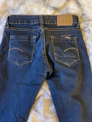 G-Star 3301 skinny jeans blå - Snygga blå G-Star 3301 jeans med tydliga kontrastsömmar och klassisk femficksdesign. Modellen är skinny med låg midja och raka ben. Jeansen har detaljerade nitar och logga på bakfickan samt läderpatch i midjan. Perfekta för en cool och avslappnad stil.