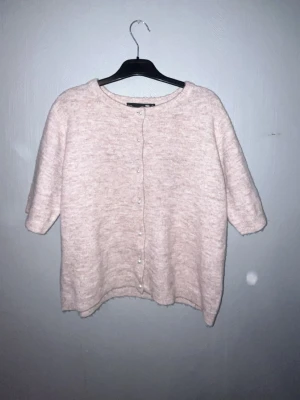 Beige stickad kofta från 157 S - Mysig beige stickad kofta från 157 i storlek S. Koftan har korta ärmar och pärlknappar framtill som ger en söt touch. Rund halsringning och mjukt material som känns skönt mot huden. Perfekt att slänga på sig när det är lite kyligt ute.